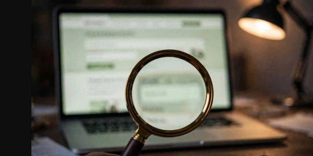 Magnifying glass over a blurred pharmacy website on a laptop, checking UK online pharmacy registration