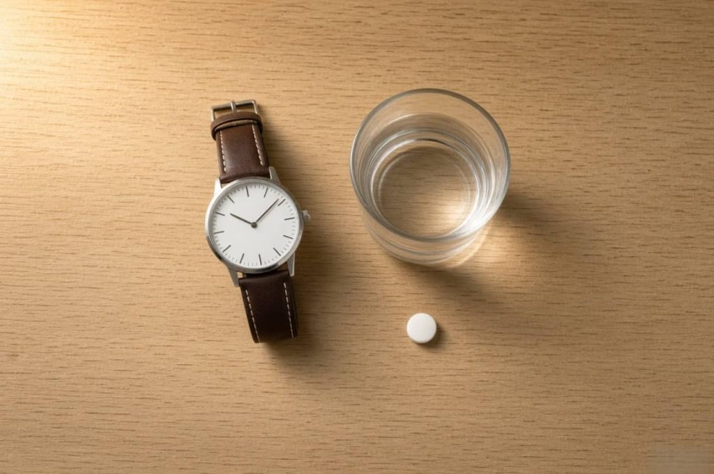 Wristwatch, glass of water and a plain white tablet on a bedside table, timing before sexual activity